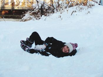 Portrait of happy girl lying down on snow covered field