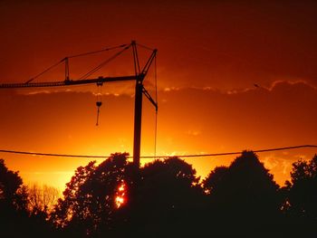 Low angle view of silhouette cranes against orange sky