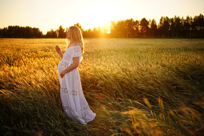 Rear view of woman standing on field against sky during sunset