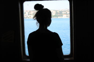 Rear view of woman looking at sea through window