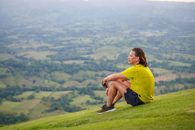 Full length of man sitting on landscape against mountains