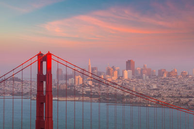 Suspension bridge in city against sky during sunset