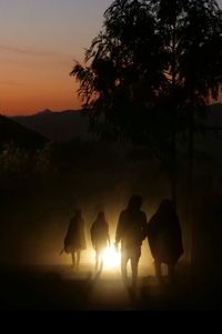 Silhouette people walking on road against sky during sunset