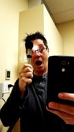 Surprised woman holding otoscope while taking selfie through smart phone