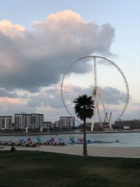 Ferris wheel at beach against cloudy sky