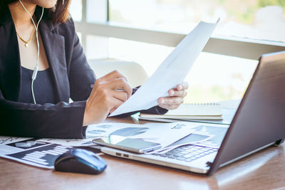 Midsection of businesswoman analyzing documents at desk in office