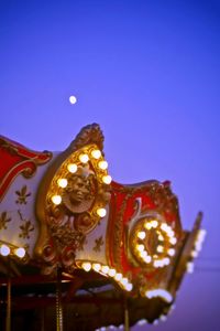 Low angle view of illuminated carousel against clear blue sky