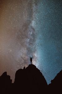 Low angle view of silhouette person standing on mountain against star field