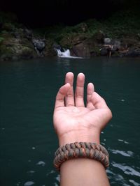 Cropped hand of man gesturing against lake