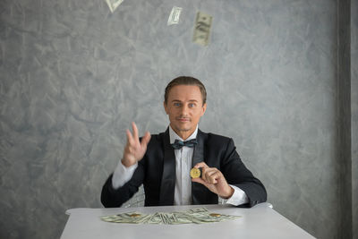 Businessman holding money while standing against wall