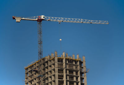 Low angle view of crane by building against clear sky