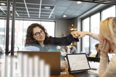 Smiling woman giving fist bump to colleagues in office