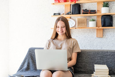 Young woman using phone while sitting on laptop