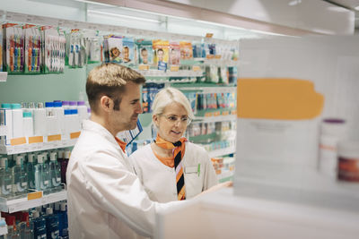 Confident pharmacists standing amidst racks in medical store