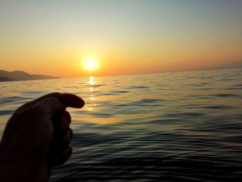 Person hand by sea against sky during sunset