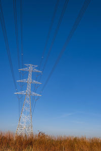 Electric pole and electric cable on the field in the countryside with blue sky.