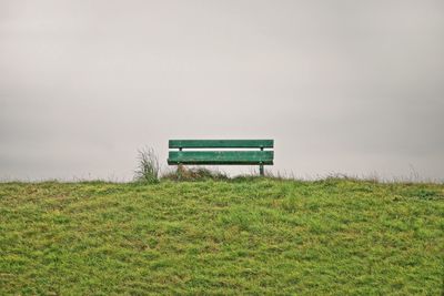 Empty bench on field against sky