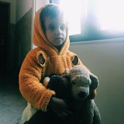 Girl wearing sweater with toy looking away while standing at home