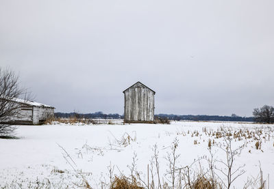 Barn on field by buildings against sky during winter