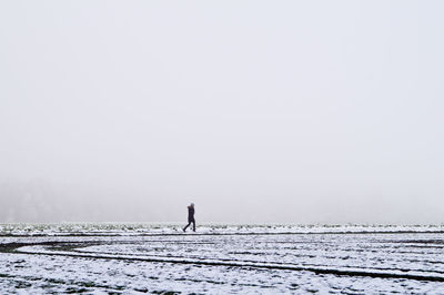 Woman walking on snow covered field in foggy weather