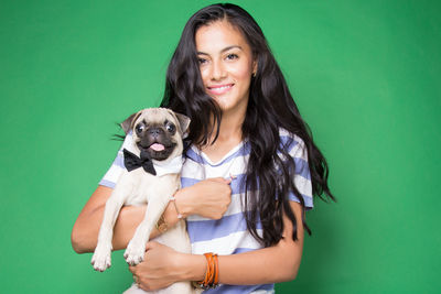 Portrait of smiling young woman holding dog over green background