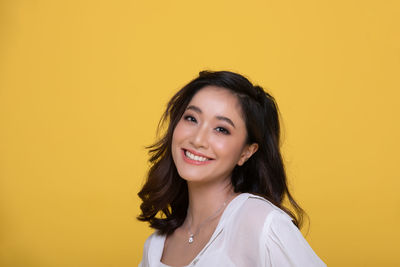 Portrait of a smiling young woman against yellow background