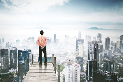 Rear view of man looking at city buildings against sky