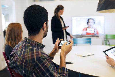 Businessman holding smart phone while attending video conference in board room