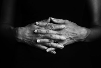 Close-up of hands clasped against black background