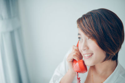 Close-up of young woman talking on telephone against wall