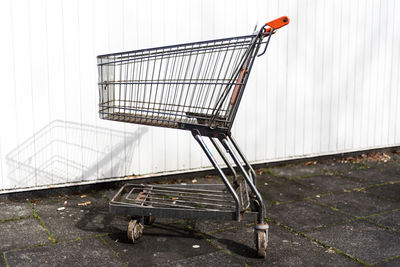 Close-up of shopping cart on sidewalk against white wall