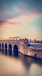 Arch bridge over river against sky during sunset