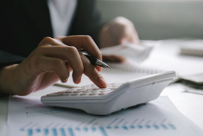 Close up of businessman or accountant hand holding pen working on calculator to calculate business 