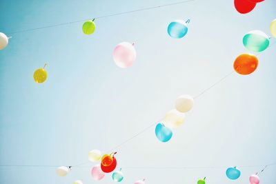 Low angle view of multi colored balloons hanging on rope against clear sky