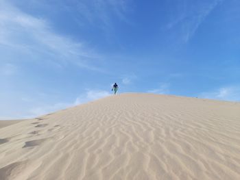 Man on sand dune in desert against sky