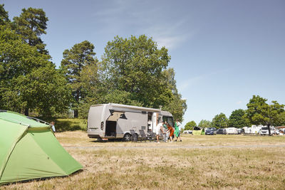 Family arranging chairs by camper van while standing on field at trailer park against sky