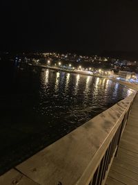 Illuminated city by sea against sky at night