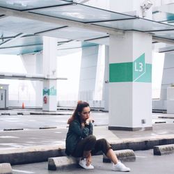 Woman sitting on rock against parking lot