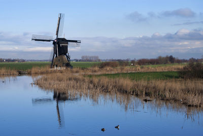 Traditional windmill on field by lake against sky
