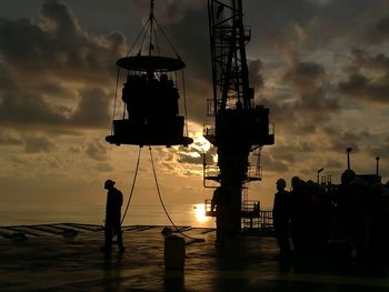 Silhouette workers standing against sky during sunset