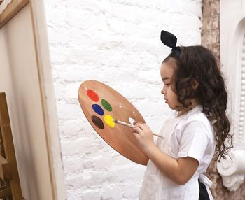 Cute girl with a paint palette and a brush. little painting artist.