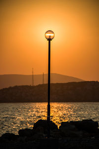 Street light by sea against sky during sunset