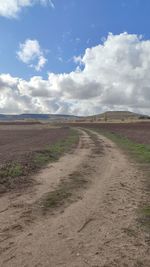 Dirt road amidst field against sky