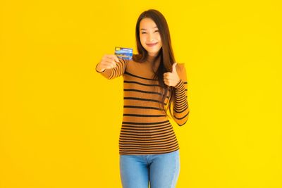 Beautiful young woman using smart phone against yellow background