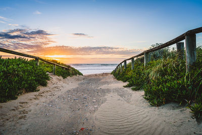 Walkway at beach against sky during sunset