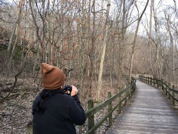 Rear view of woman with binoculars on boardwalk at forest