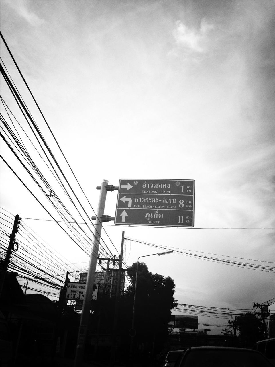 low angle view, sky, built structure, communication, text, architecture, power line, building exterior, electricity pylon, connection, silhouette, cable, western script, outdoors, tree, electricity, no people, city, cloud, cloud - sky