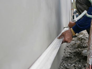 Hand of a construction worker holding on a long wooden screed during the cement plastering process