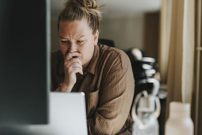 Worried female business professional sitting with laptop at office