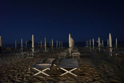 Chairs on beach against clear sky at night